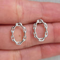 Silver hoop earrings held between fingers on a neutral background