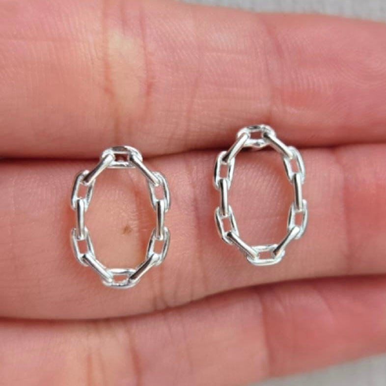 Silver hoop earrings held between fingers on a neutral background