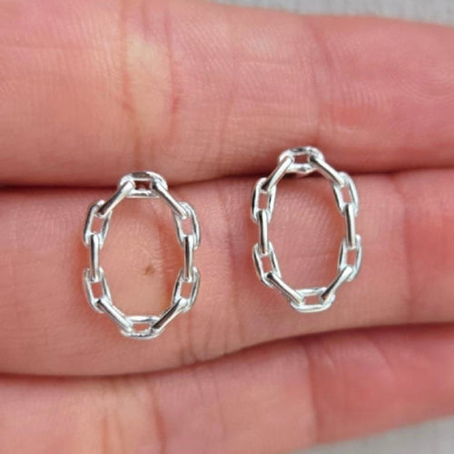 Silver hoop earrings held between fingers on a neutral background