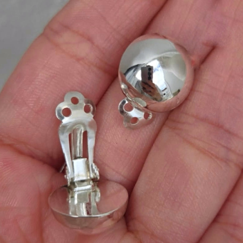 Close-up of silver earring components held in a hand.