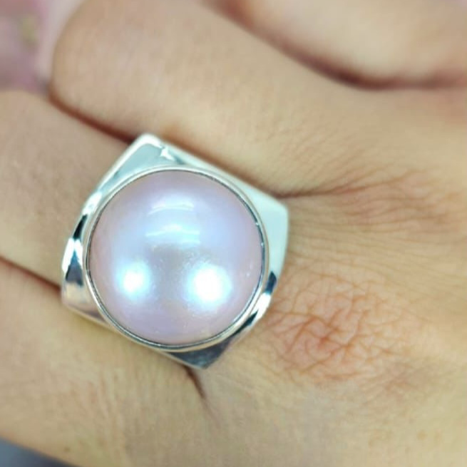 A 19mm pink mabe pearl ring set in sterling silver, displayed on a person's finger.