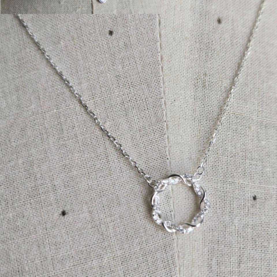 Silver necklace with a circular pendant on a textured beige background