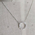 Silver necklace with a circular pendant on a textured beige background
