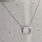 Silver necklace with a circular pendant on a textured beige background