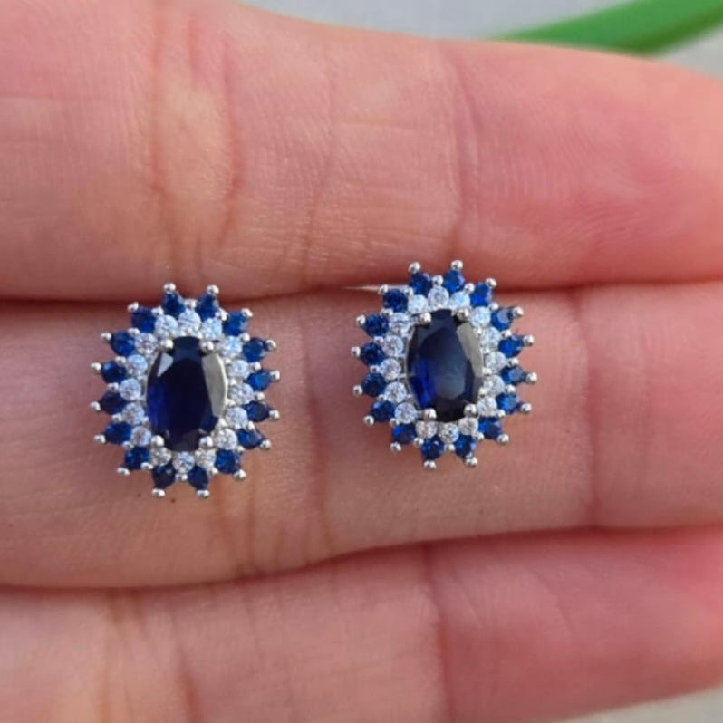 Pair of silver earrings with blue gemstones held between fingers.