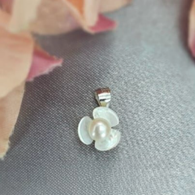 A sterling silver pendant featuring a mother of pearl flower with a freshwater pearl center, displayed against a fabric background.