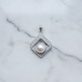 Pearl pendant with silver frame on a light gray fabric background