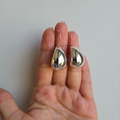 A pair of large teardrop-shaped earrings made from sterling silver, displayed on a person's hand.
