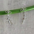 Silver floral earrings on a green stick against a gray background