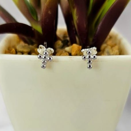 A pair of sterling silver cross studs earrings placed on a white pot with plants in the background.