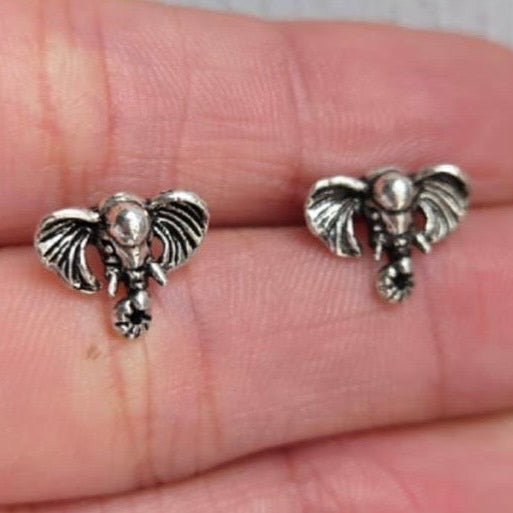 Silver elephant earrings held between fingers on a light background