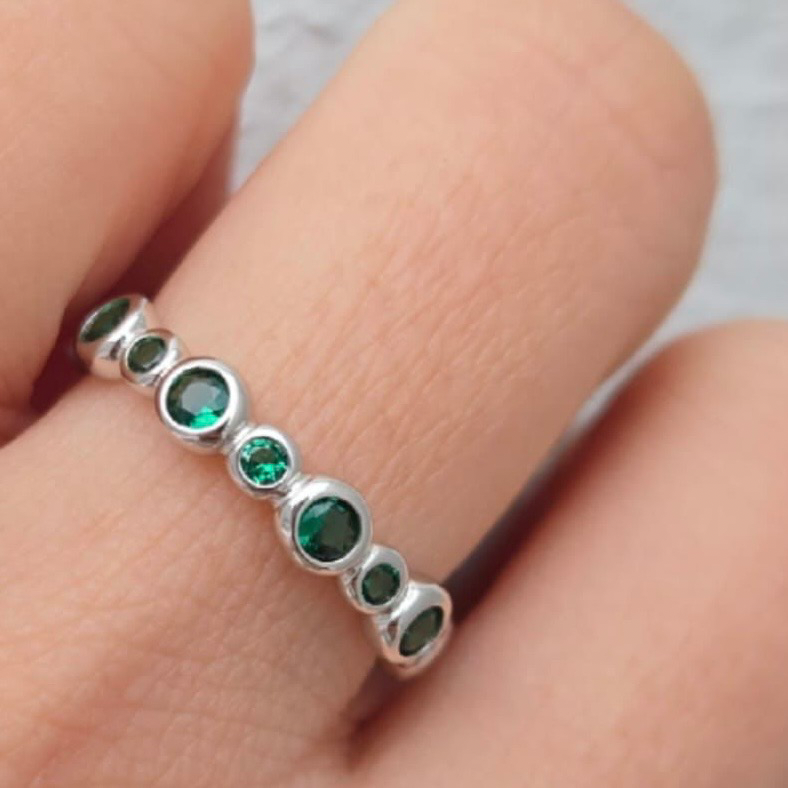 Silver ring with green gemstones on a finger against a neutral background