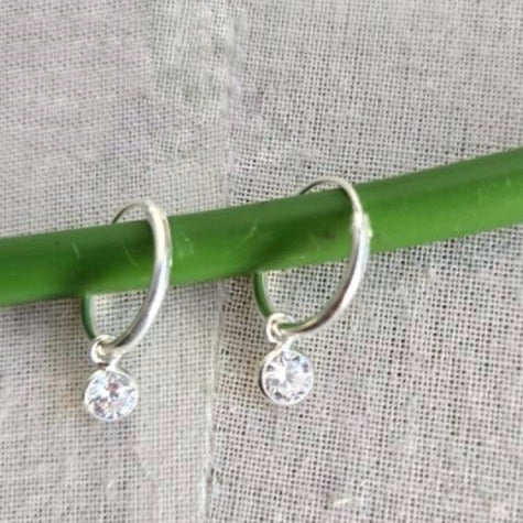 Silver hoop earrings with clear gemstones on a green stick against a textured fabric background
