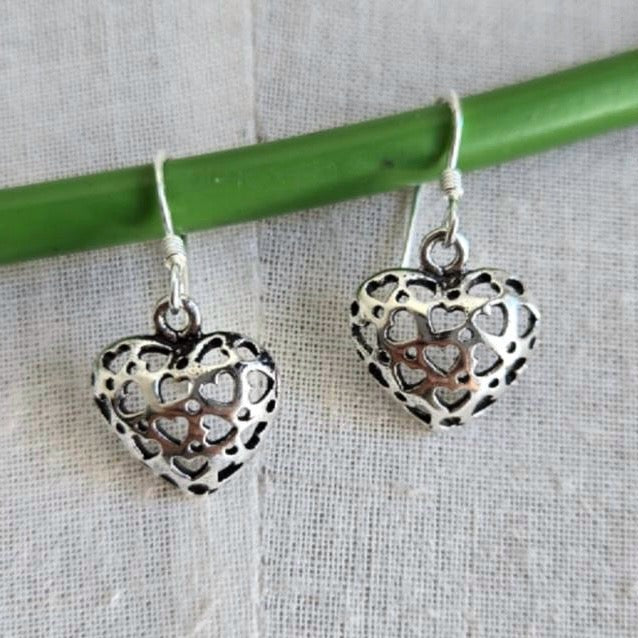 Silver heart-shaped earrings on a green stick against a textured fabric background