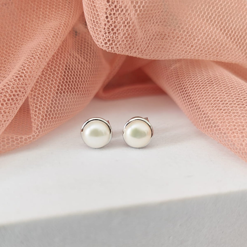 Pearl stud earrings on a white surface with pink fabric in the background