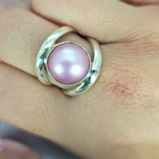 A pink Mabe pearl ring in a sterling silver setting, displayed on a person's hand.
