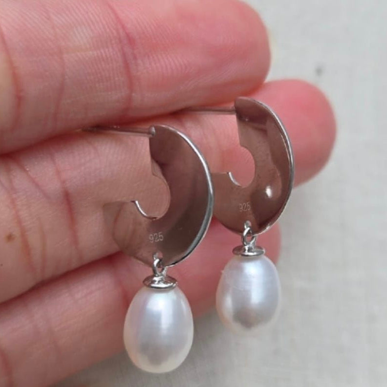 Silver earrings with pearl drops held between fingers on a light background