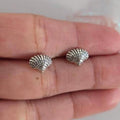 Silver shell-shaped earrings on a person's hand
