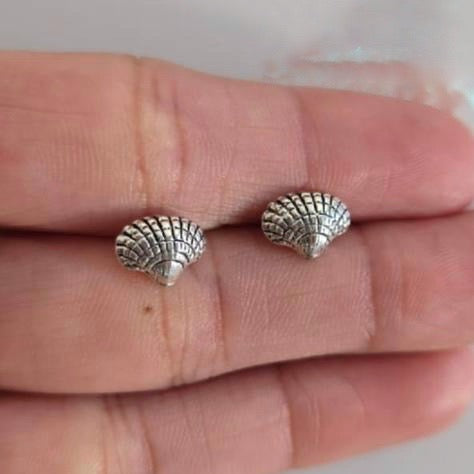 Silver shell-shaped earrings on a person's hand