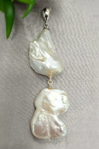 A double pearl pendant with a silver chain, one pearl is white and the other is beige, both with gold accents.