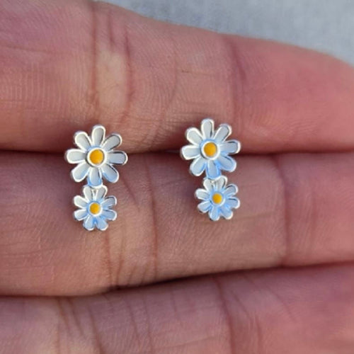 Silver daisy earrings on a hand with a neutral background