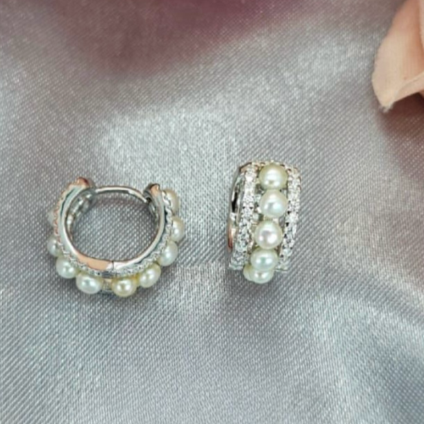 A pair of sterling silver huggies with a cascade of freshwater pearls, displayed on a textured surface.