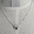 Silver necklace with a heart pendant on a mannequin.