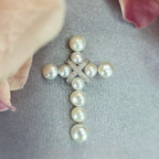 A sterling silver cross pendant with ten freshwater pearls and a cubic zirconia detail on a chain, placed against a soft floral background.