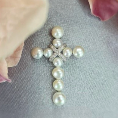 A sterling silver cross pendant with ten freshwater pearls and a cubic zirconia detail on a chain, placed against a soft floral background.