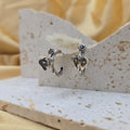 Pair of silver earrings on a stone display block with a soft yellow background
