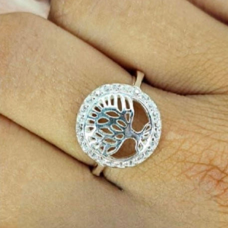 A sterling silver ring featuring a tree of life design, worn on a person's finger.