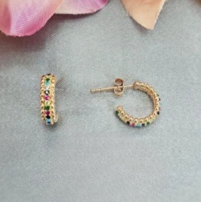 Gold hoop earrings with colorful gemstones on a gray surface with pink flowers.