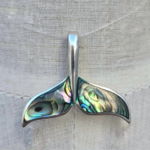Silver pendant with abalone shell design on a textured fabric background
