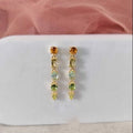 Gold earrings with green gemstones on a white card with pink fabric background