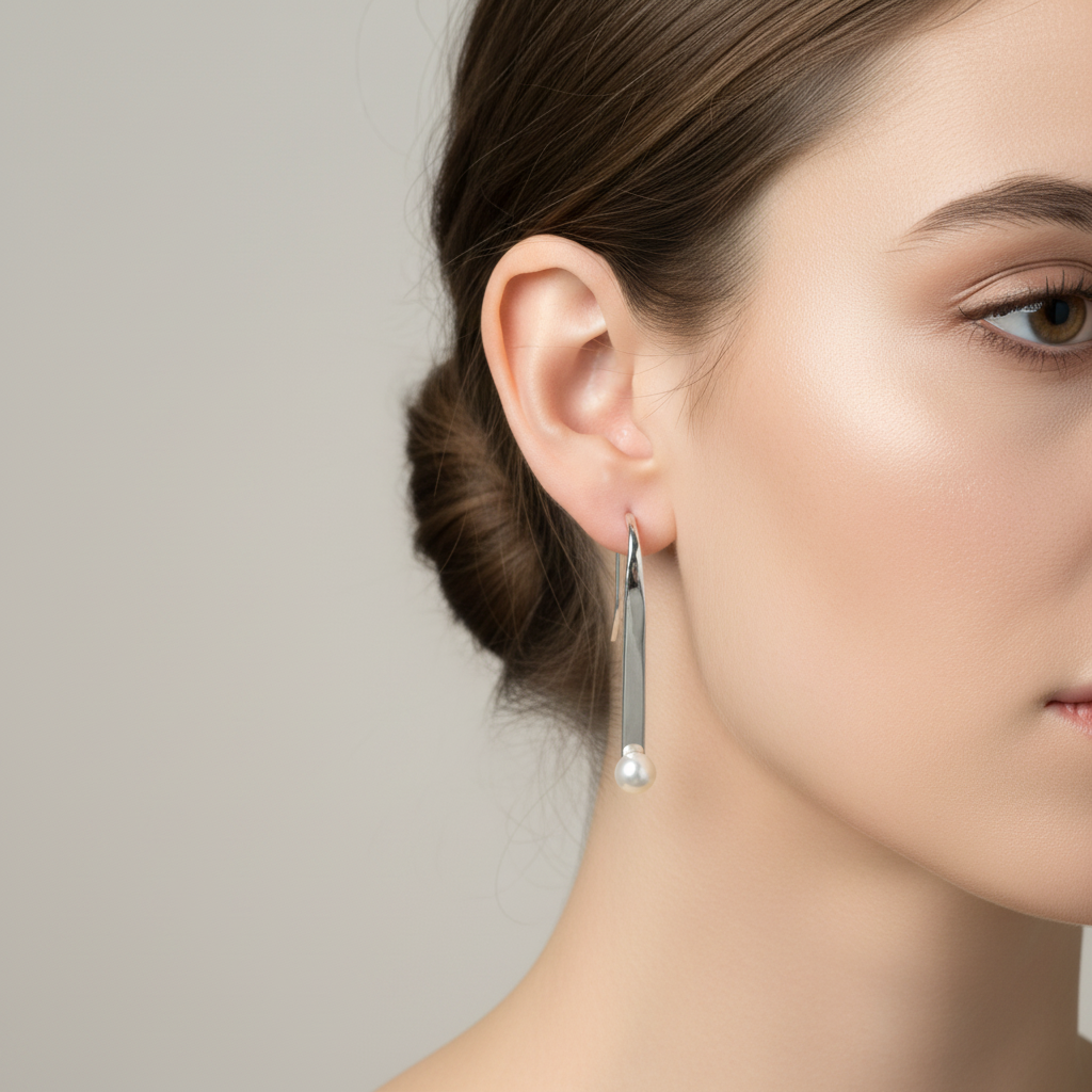 A pair of modern silver bar earrings with freshwater pearls on ends, displayed in a white pot with green plant leaves.