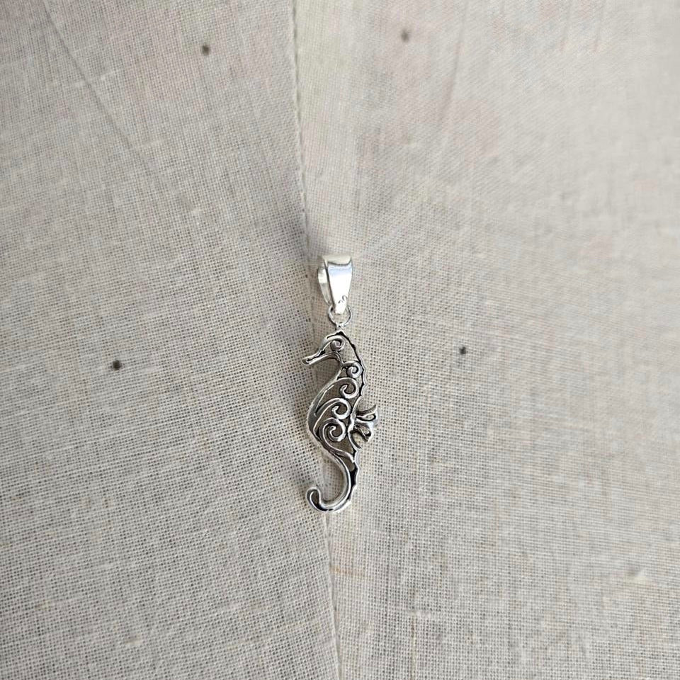 Silver seahorse pendant on a light gray fabric background