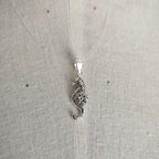 Silver seahorse pendant on a light gray fabric background