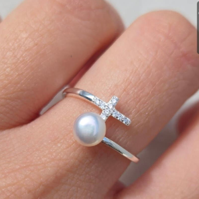 Silver ring with a pearl on a finger against a neutral background