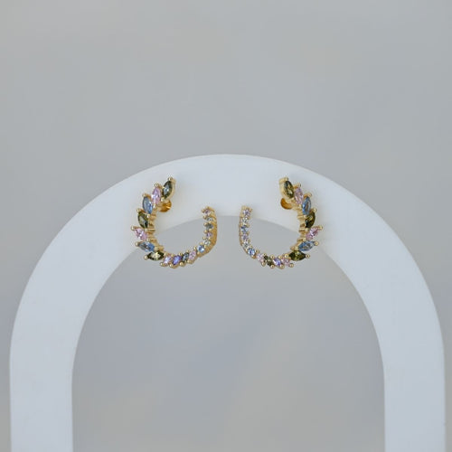 Pair of gold hoop earrings with colorful stones on a white stand against a light gray background