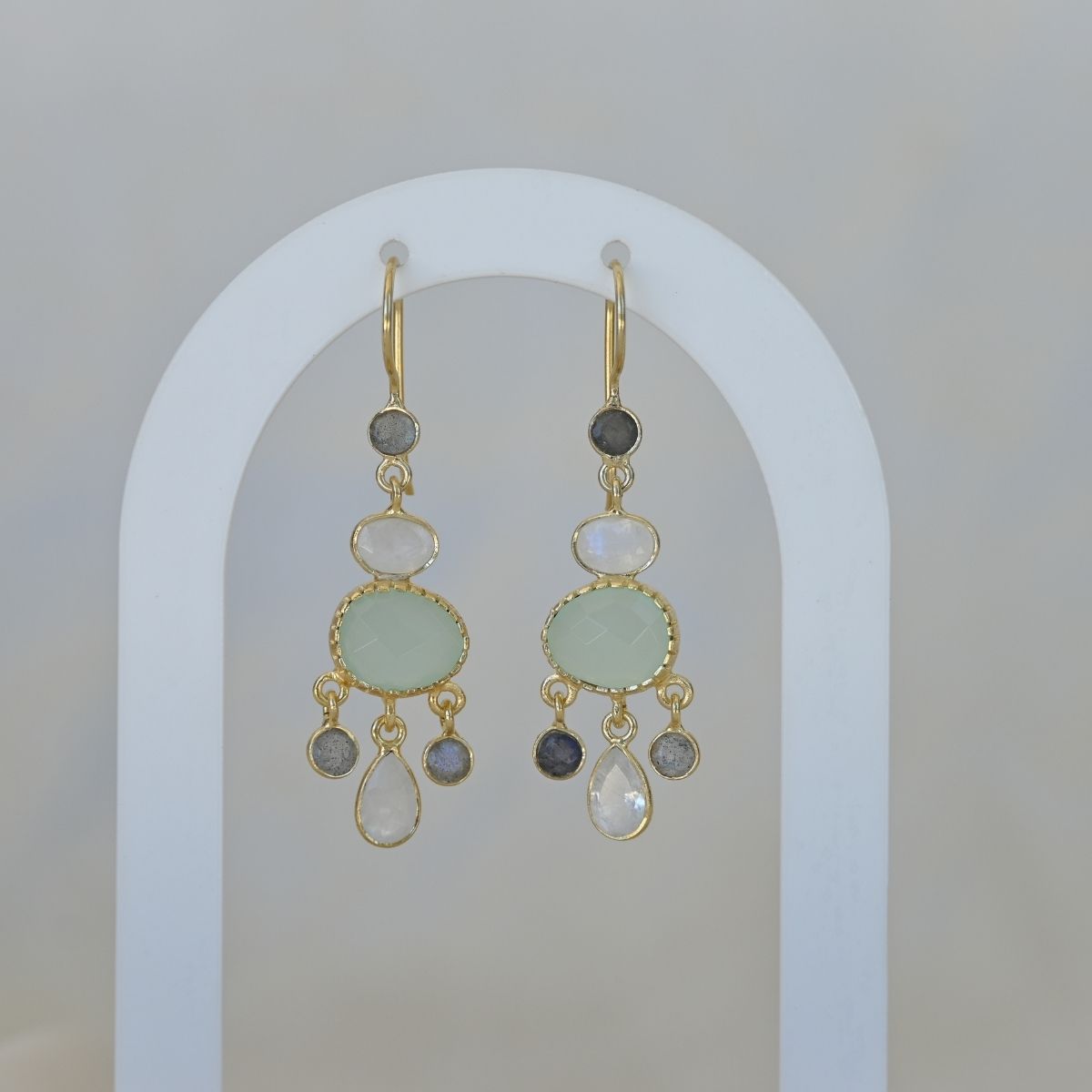 Gold earrings with green and gray stones on a white arch background