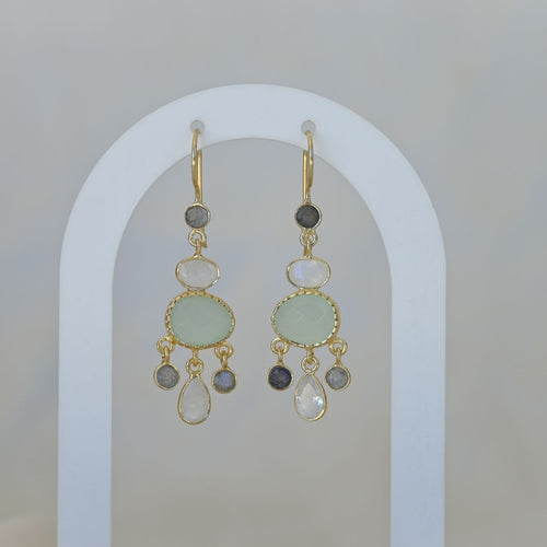 Gold earrings with green and gray stones on a white arch background