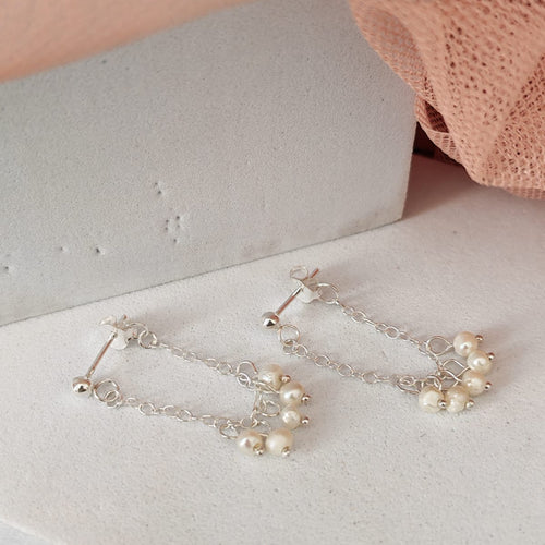 Silver earrings with pearls on a white surface