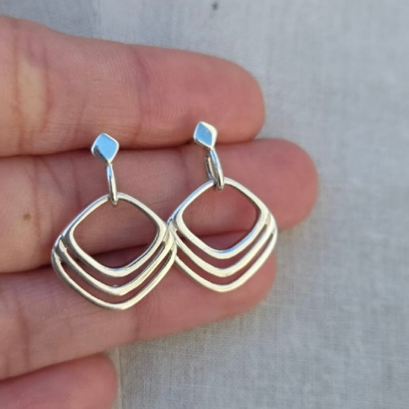 Silver earrings held between fingers against a neutral background