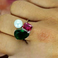 An image displaying a sterling silver ring with an emerald green teardrop, a red rectangular cubic zirconia, and a large freshwater pearl on a person's hand.