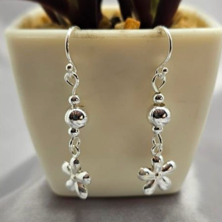 A pair of sterling silver ball and flower drop earrings placed on a surface next to a potted plant.
