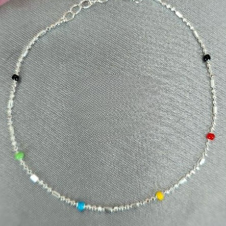 A Sterling silver bracelet with colorful drops in the links, displayed on a grey surface.