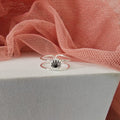 Silver ring with black stone on a white surface with pink fabric in the background