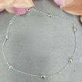 A sterling silver anklet with small balls presented on a textured background with flower petals scattered around.
