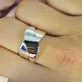 A sterling silver cross over band ring on a person's finger, with a blurred background.