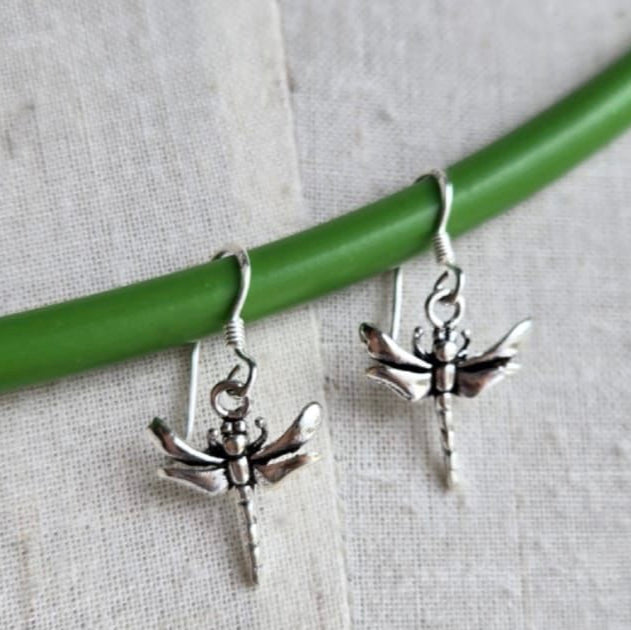 Silver dragonfly earrings on a green stick with a light gray background